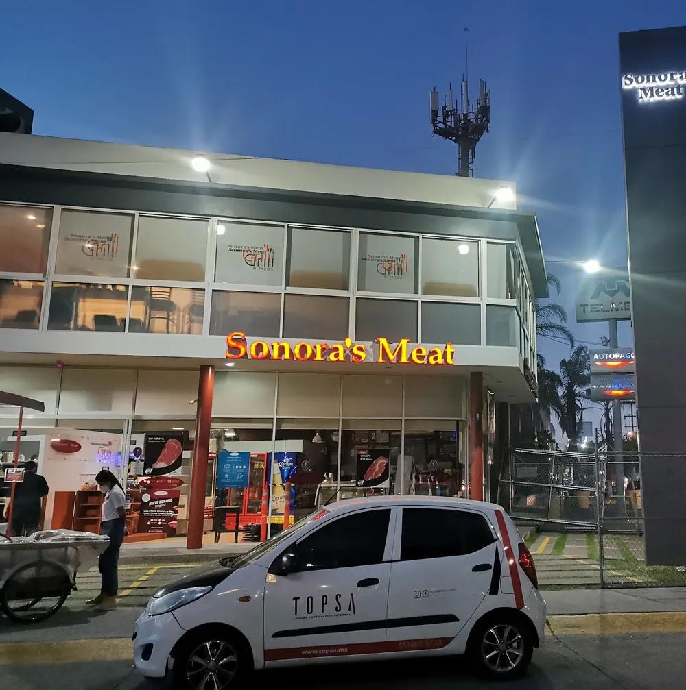 Letras iluminadas de Sonora's Meat en fachada y tótem, al anochecer