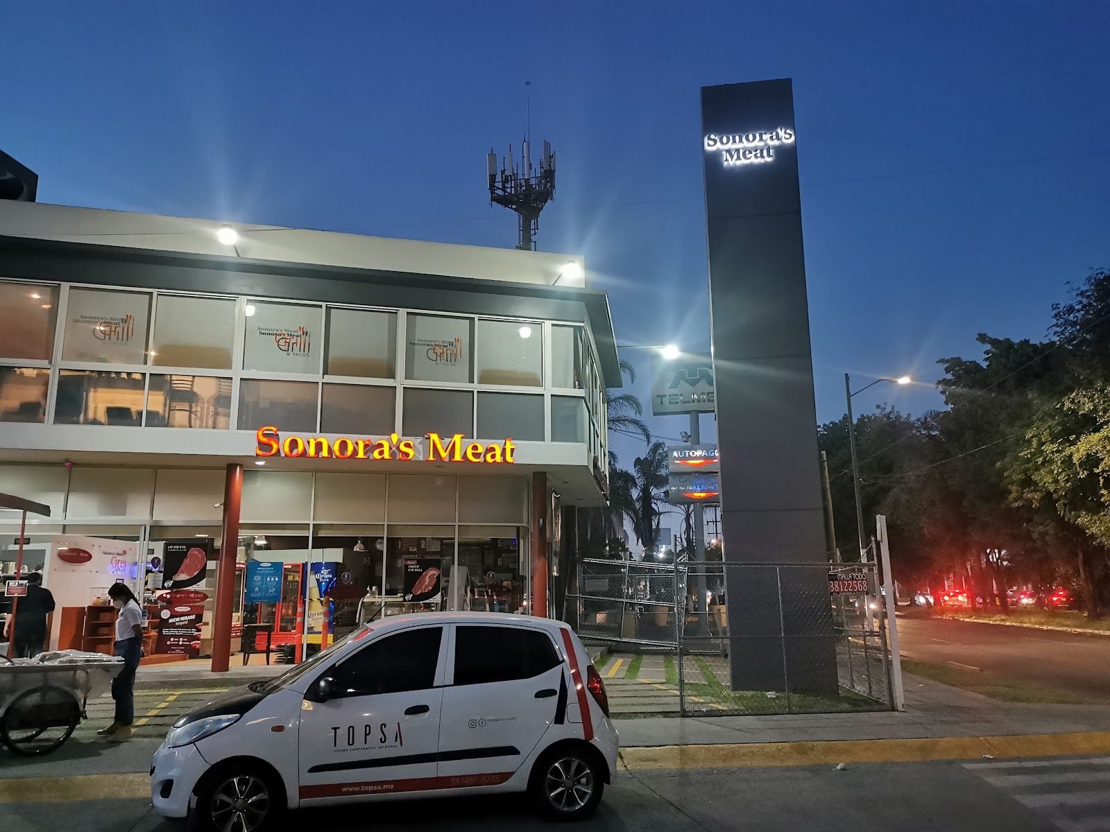 Tótem oscuro con letras iluminadas frente a un restaurante al atardecer