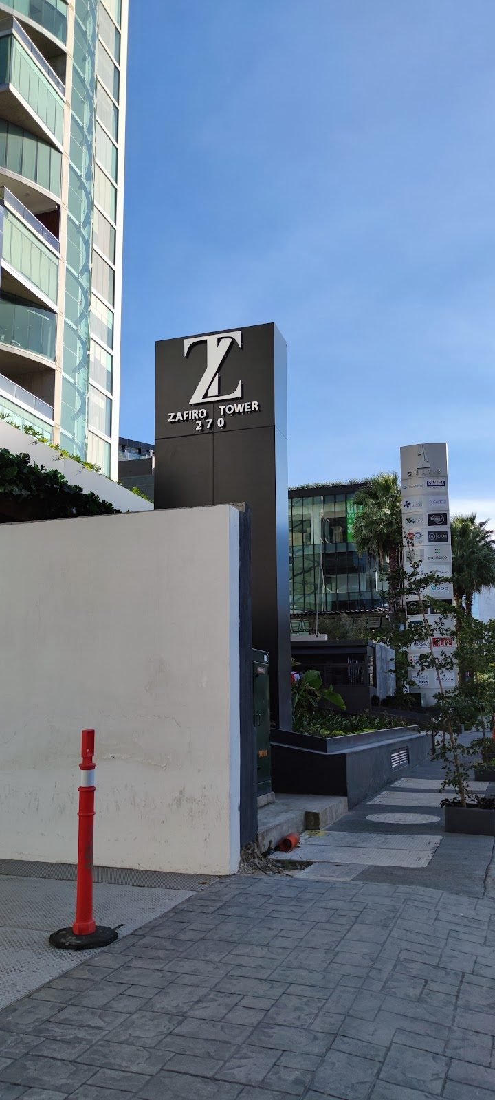 Tótem corporativo con letras metálicas junto a torres de departamentos